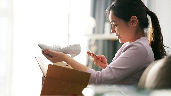 亚洲女性消费者打开纸箱得到邮包鞋在网上购买