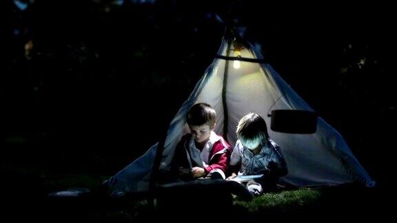 可爱的小弟弟们晚上在帐篷里玩平板电脑和电话