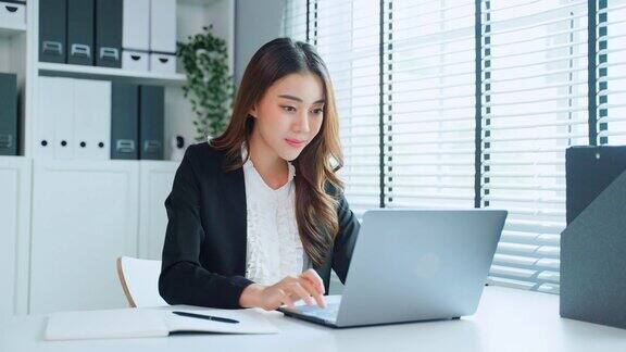 疲惫迷人的亚洲女商人在工作桌上看着许多文件工作忙碌的女员工由于工作到很晚在办公室的电脑桌上放着工作文件感到疲惫头痛