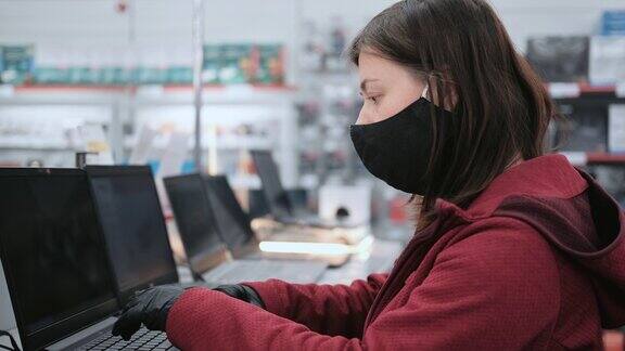 戴着面具和手套的女孩在一家电子商店买了一台笔记本电脑