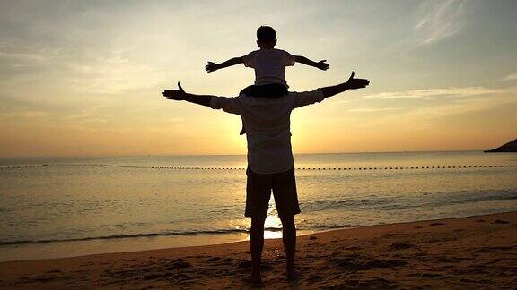 日出时父亲和儿子站在海滩上