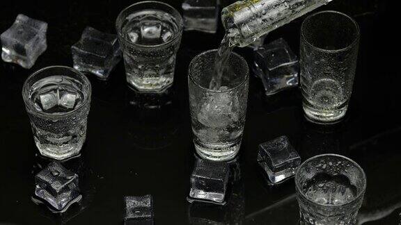 酒保将冰冻的伏特加从瓶子倒入小酒杯黑色背景下的冰块