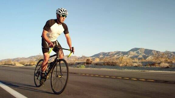 年轻的健康男子在沙漠道路上骑自行车在日落