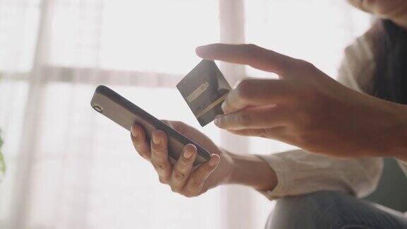 一名年轻的亚洲女性在家里用智能手机刷信用卡网购