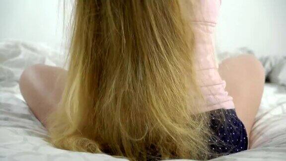 金色长发的女孩在早上坐在床上梳理她的长发