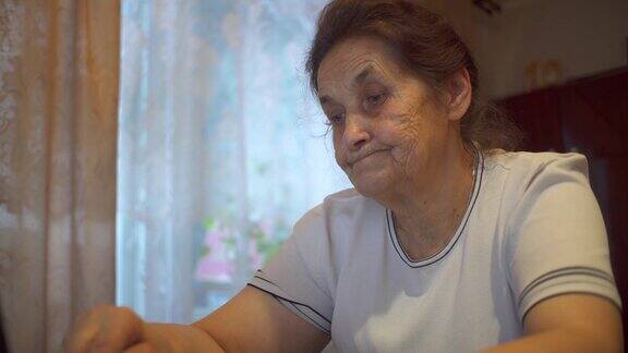 一位上了年纪的妇女坐在她公寓的笔记本电脑前她一边看显示器一边上网