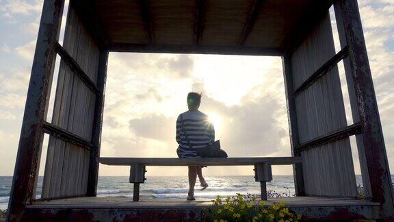 日落时分坐在海边长椅上的女孩