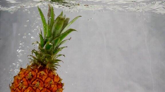 用慢动作将菠萝浸入一个充满气泡的水容器中孤立在白色背景上的菠萝