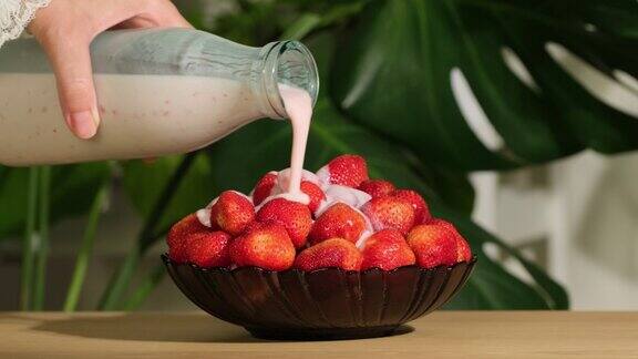 从瓶子里把酸奶倒在草莓上慢动作将酸奶倒入碗中成熟的红草莓中