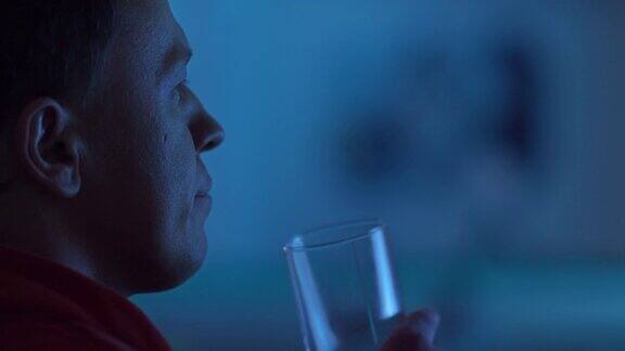 男人晚上坐在电视机前喝着苏打水看电影彩色的反光特写镜头