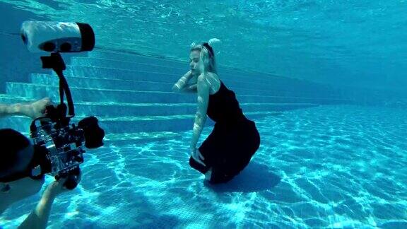 水下摄影师在游泳池底部拍下了一个身穿黑色连衣裙、头上戴着白色犄角的金发女孩动漫真人秀缓慢的运动水下摄影4k25fps