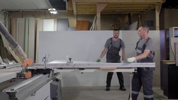 家具制造车间两名工人正在把刨花板放到切割机上