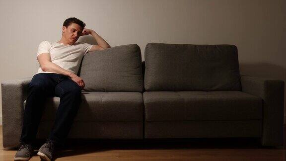 一个沮丧的年轻人坐在灰色的沙发上