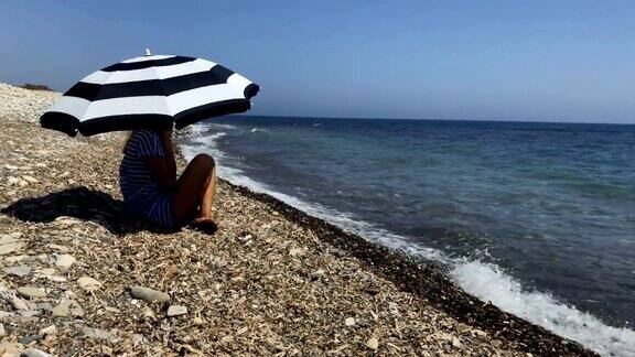 拿着伞的女人坐在海边欣赏美丽的海景
