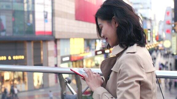 在慢镜头中一个年轻漂亮的亚洲女人在城市中使用手机