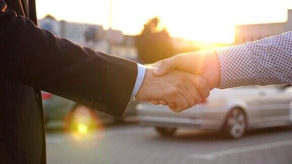 两个商人互相握手后面停着车经理或经销商与客户之间的握手伙伴们在外面握手特写慢动作侧视图
