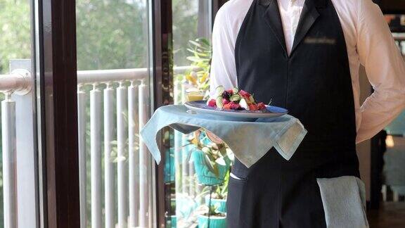 服务员端着一盘美味的沙拉沿着全景玻璃窗递给客户一个穿着白衬衫黑围裙的侍者在一家现代化的餐馆里忙碌地服务着