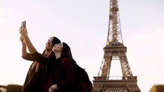 阳光明媚的法国巴黎两个美丽的旅行女性在埃菲尔铁塔附近用智能手机拍照