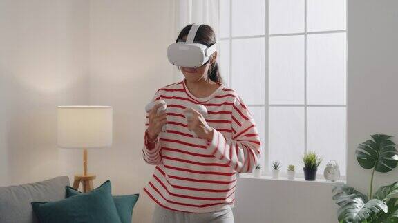 年轻女子戴着VR头戴式设备在家中客厅体验模拟数字世界拳击姿势玩动作模拟游戏手机app