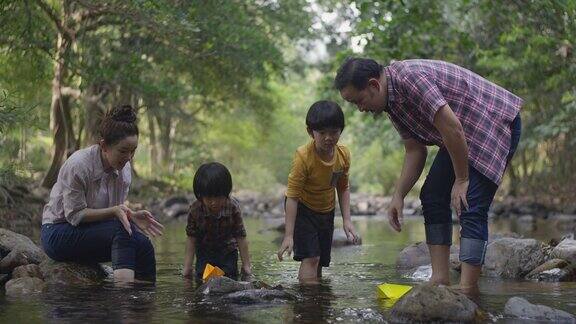 一个亚洲家庭在河边玩纸船