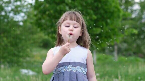 一个可爱的小女孩在春天的公园里吹蒲公英快乐的孩子在户外玩得开心
