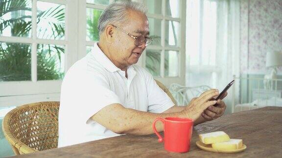 一名亚洲老人在吃早餐时使用智能手机