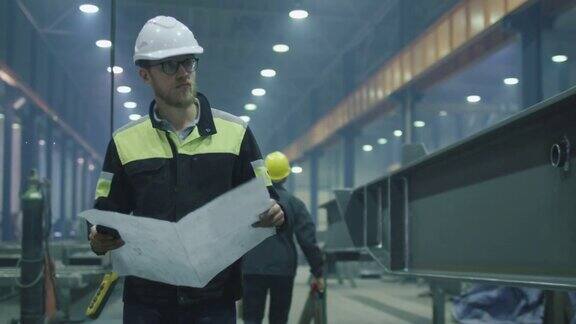 戴安全帽的工程师正在带着蓝图穿过一个重工业工厂