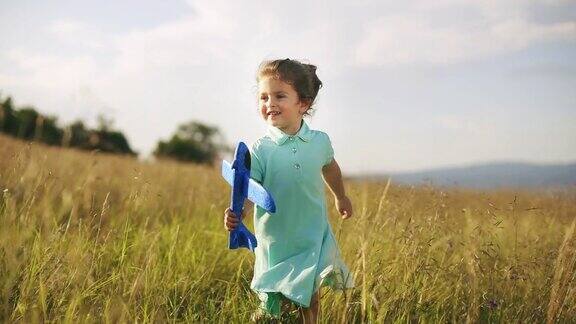 美丽的蹒跚学步的小女孩和她的飞机玩具在日落草地上奔跑慢动作
