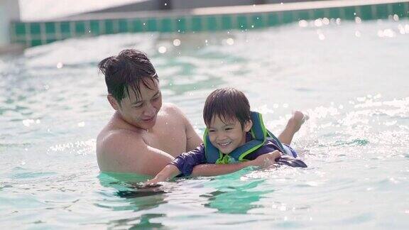 年轻的亚洲父亲教他的儿子在游泳池游泳