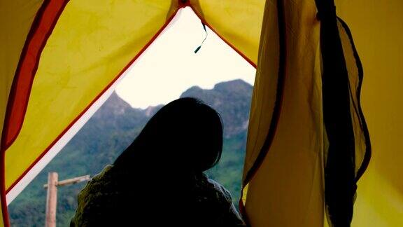 在假期的日落时分女人打开帐篷走出去呼吸山景的新鲜空气