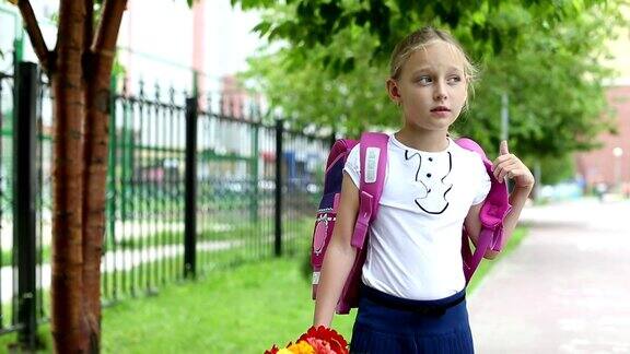 年轻漂亮的女孩站在学校附近的背包和鲜花晴天回到学校女学生去学习小学户外绿树成荫风姑娘带着花站在学校