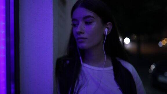 女人听着音乐在夜晚的街道上靠在墙上放松