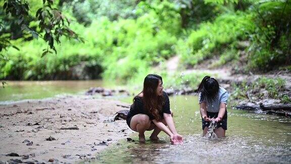 一位亚裔中国妇女和她的女儿在河边玩水花