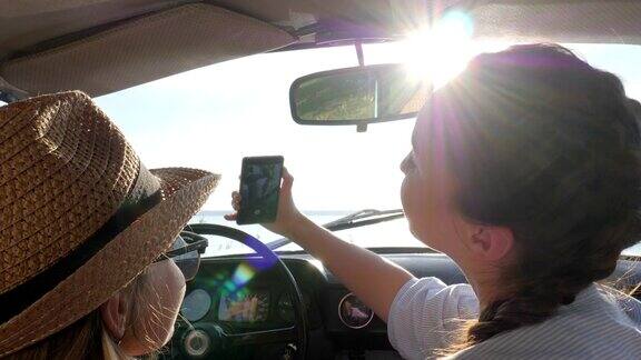 快乐旅程女孩们在阳光下在车里自拍年轻女孩坐在汽车里用手机拍照女朋友们自拍