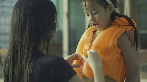 美丽的年轻母亲在女儿游泳前帮她穿上救生衣