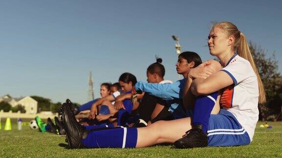 女子足球队在足球场上训练前伸展双腿4k