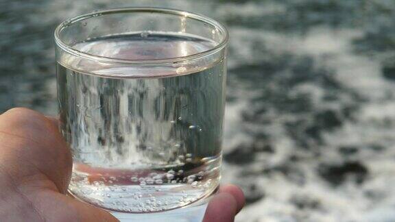 在瀑布旁一名男子拿着一个盛满水的玻璃杯喝水
