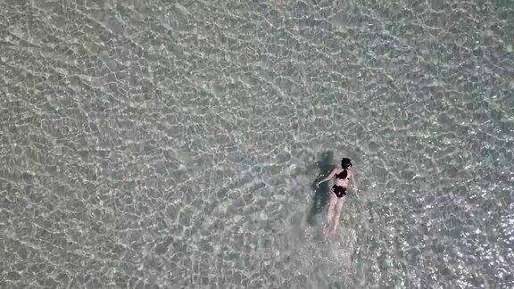 鸟瞰图亚洲妇女游泳和漂浮在水晶清澈的水海上