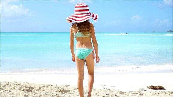 可爱的小女孩戴着大帽子走在白色的沙滩上