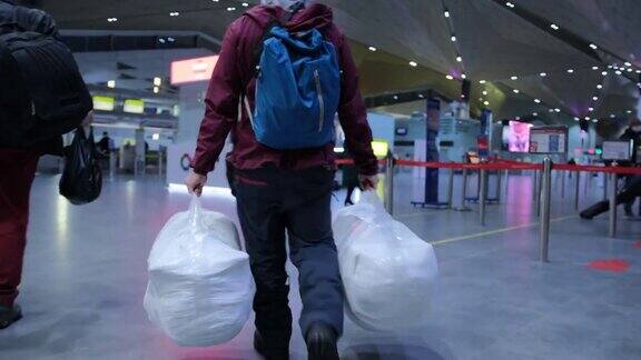 一名男子在机场办理登机手续时手里拿着两个大袋子里面包着塑料布