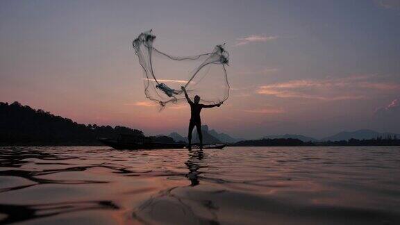 慢镜头剪影渔民抛出渔网在日落与船在湖渔民的生活方式泰国华富里以、亚洲