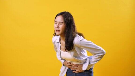 一名亚洲妇女胃痛孤立地站在黄色背景上