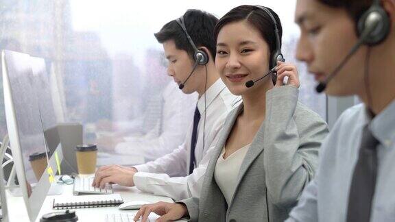 微笑的亚洲女性呼叫中心接线员与电话营销团队