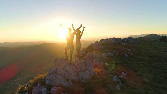 照片:日落时分一对徒步旅行者在到达顶峰后伸出手臂