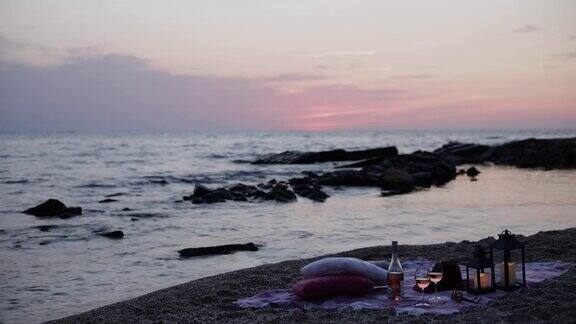 夏季海上日落浪漫的海滩野餐一瓶酒玻璃杯蜡烛格子呢和枕头