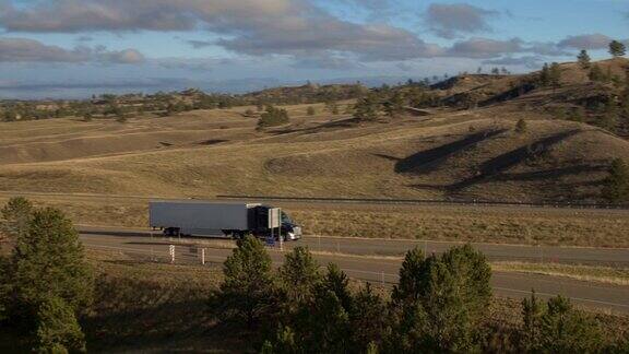 空中摄影:在阳光明媚的丘陵地带拖着货物的半挂卡车沿着繁忙的乡村公路行驶