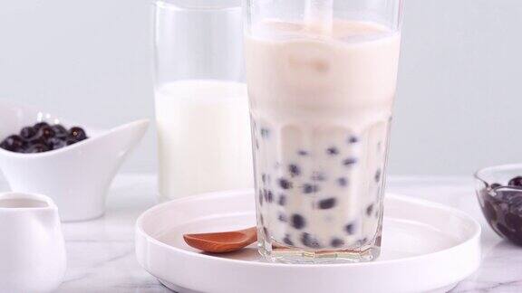 搅拌可口的台湾流行饮料木薯珍珠泡奶茶在玻璃杯上明亮的大理石桌子白色托盘自制4k拍摄视频