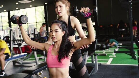 一位亚洲私人教练正在健身房里用哑铃训练一位健美女士