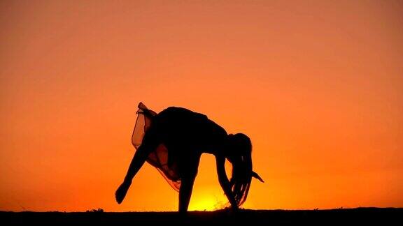 一个年轻女孩的剪影在夕阳下翻筋斗