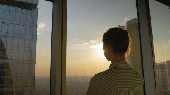 透过摩天大楼的窗户看日落的女人的背影